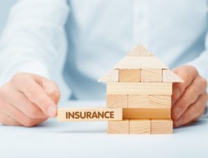 a man building a mini house on a table using jengga pieces with one of the blocks saying "insurance"